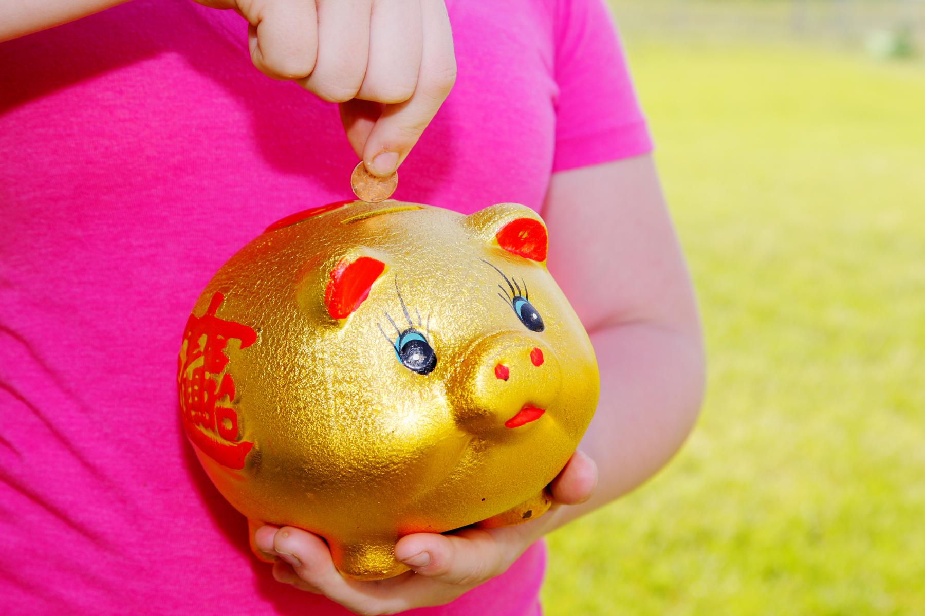 File:Girl Purring Money Into Piggy Bank.jpg - a little girl holding a gold pig toy